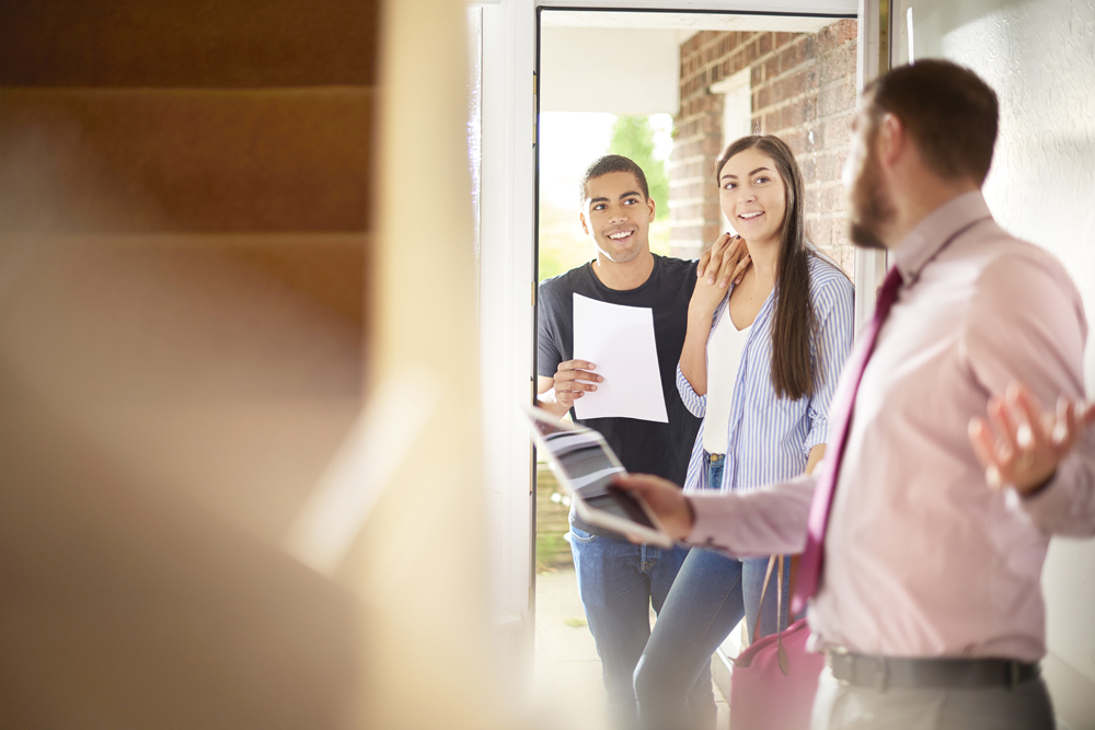 a young couple view a property guided by an estate agent. They are standing in the hallway of house and chatting about the paperwork that they are holding .