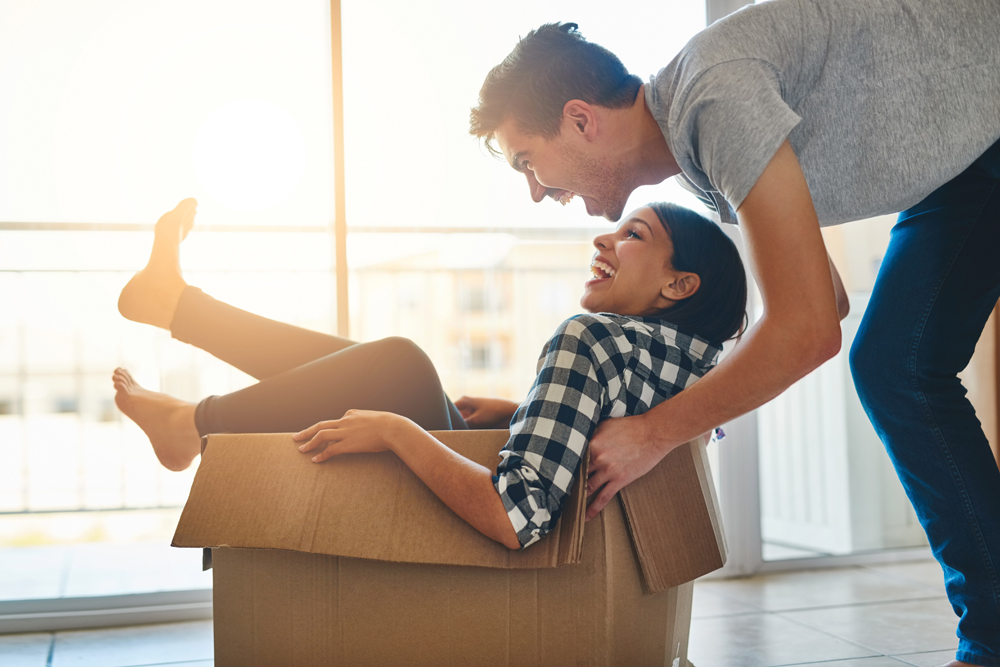 Shot of a young man pushing his girlfriend around in a box while they move into their new home together